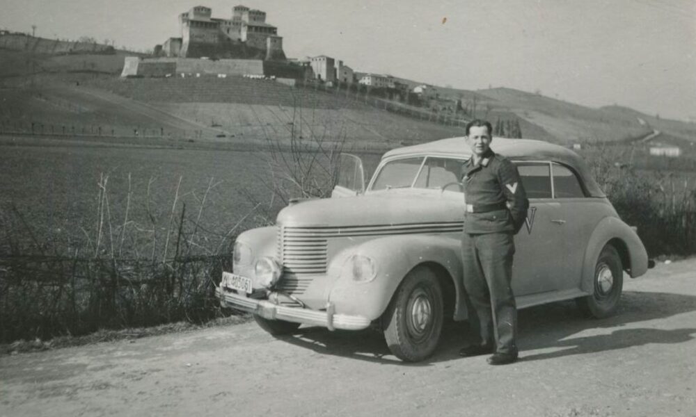 Uomo fuori da un auto con sfondo paesaggistico. Fonte: Direzione Regionale Musei Emilia Romagna. Paesaggi culturali